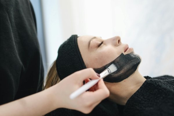 putting on organic vegan charcoal face mask on a customer in a spa.